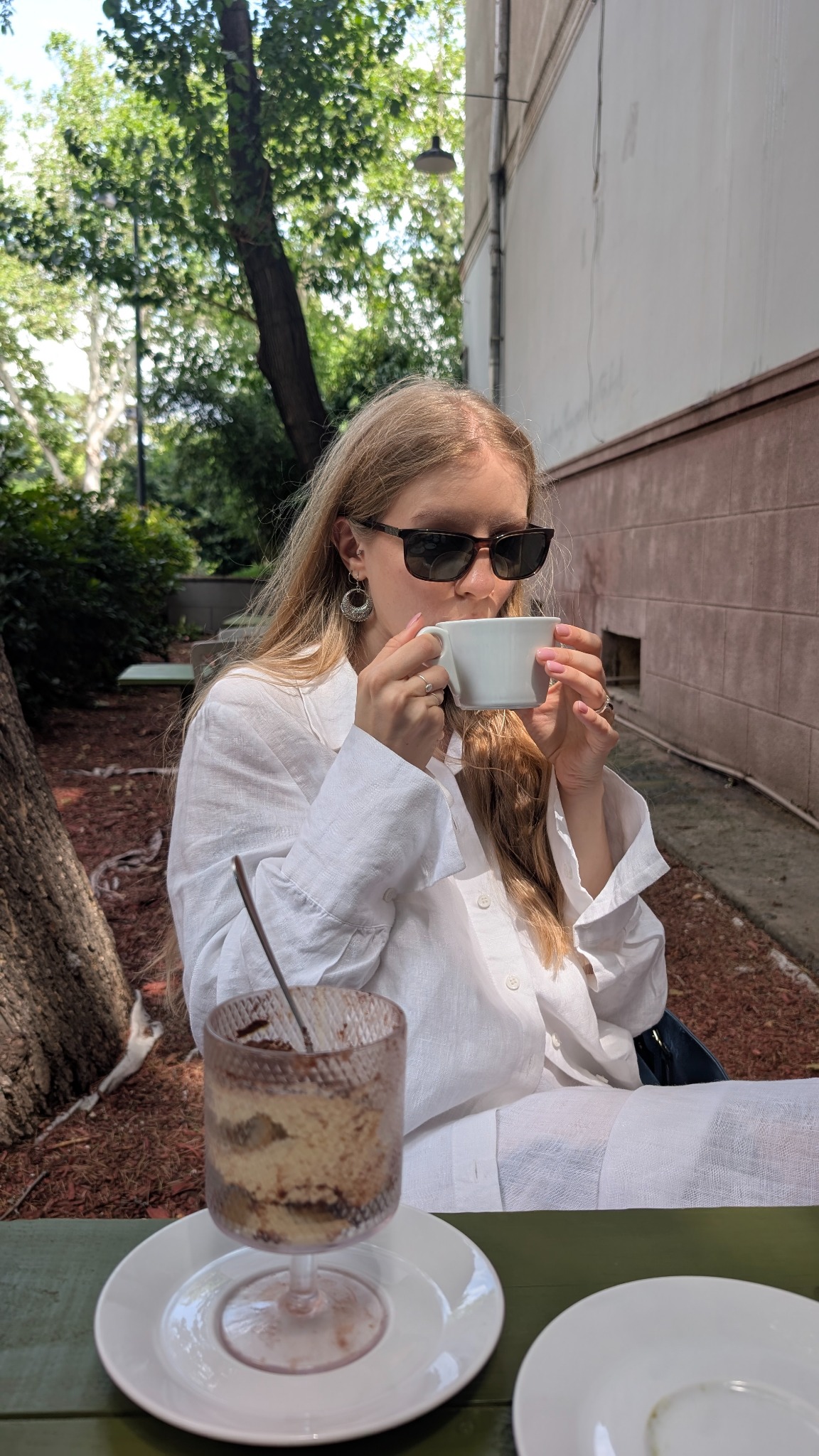 Vero sitting outdoors in a white outfit, drinking coffee in the sunlight.
